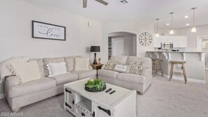 A modern living room with a sectional sofa, a coffee table, and a kitchen area in the background. - Cozy condo in Litchfield Park (Litchfield Park)