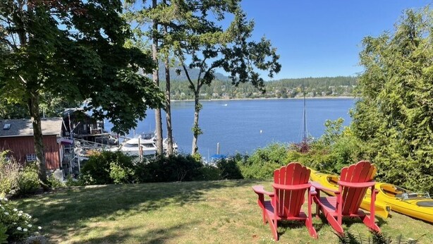 Une zone herbeuse avec deux fauteuils Adirondack rouges, placés face à un lac.