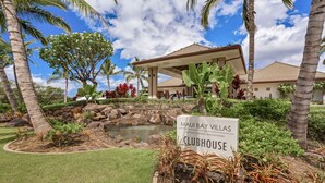 A sign for 'Maui Bay Villas Clubhouse' with a landscaped garden featuring palm trees, a small pond, and a covered seating area.