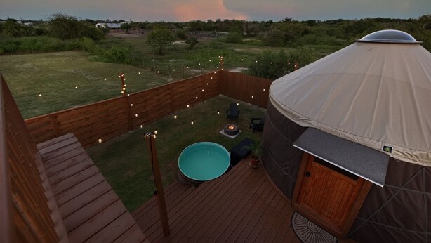 Une yourte dotée d’une terrasse en bois, d’une petite piscine et de guirlandes lumineuses.