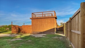 Une cour arrière clôturée, avec une structure en bois, peut-être une cabane de jeux ou un abri de jardin, et une clôture en bois qui entoure l’ensemble.