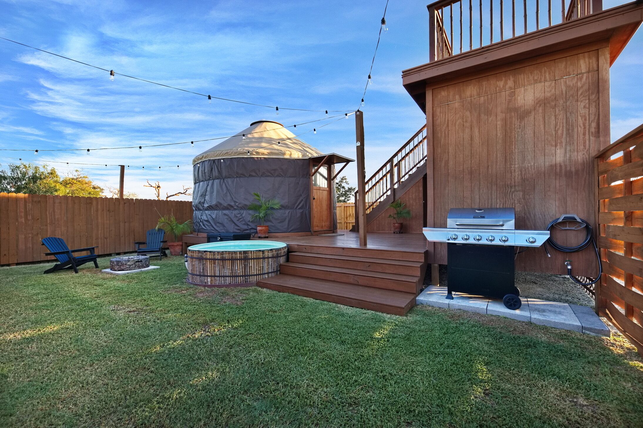 Un jardin avec un jacuzzi, un espace salon couvert, un barbecue et une terrasse en bois.
