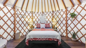 L’intérieur chaleureux d’une yourte, avec un lit, deux tables de chevet et une décoration en macramé suspendue.