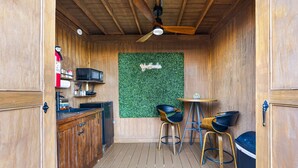 Une cuisine compacte avec des meubles en bois, un four à micro-ondes et un mur vert agrémenté d’une enseigne. On y trouve deux tabourets et une petite table.