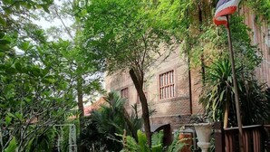 A courtyard with a brick building, a white fence, and various plants. - Ruennakornin (Bang Kruai)