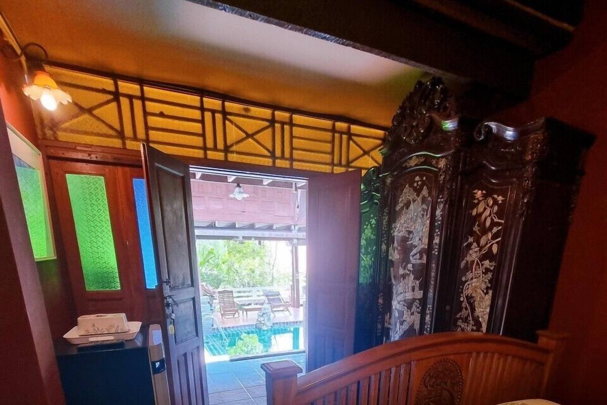 A bedroom with a bed, a wooden headboard, a nightstand, and a view of an outdoor area with a pool.