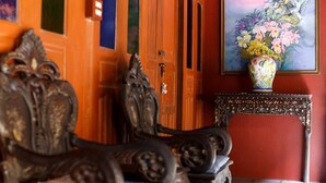 A room with ornate furniture, a wooden door, and a painting of flowers on the wall. - Ruennakornin (Bang Kruai)
