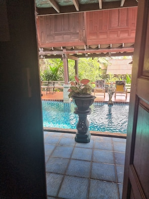 Vista de una piscina con una urna decorativa en el centro, rodeada de pavimento de baldosas y una pérgola de madera.