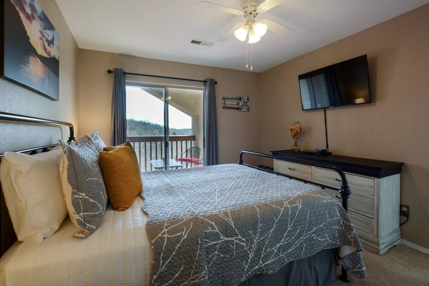 A bedroom with a bed, a desk, a TV, and a balcony with a view.