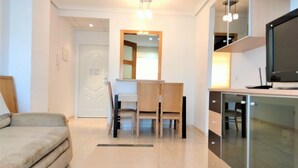 Een moderne woonkamer met een bank, een eettafel met stoelen, een keukenhoek met een televisie en een glazen kast.