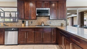 A modern kitchen with dark wooden cabinets, a stainless steel dishwasher, a built-in microwave, and a granite countertop. - Amazing 6 BRD, Pool, Theater, Billiard, Poker, and Games near the Strip (Las Vegas)