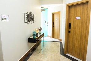 A hallway with a wooden door, a glass console table with decorative items, and framed pictures on the wall. - Fiori Suítes  (Goiânia)