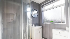 Un baño moderno con ducha cubierta por vidrio, lavamanos blanco y retrete.