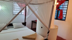 A bedroom with a bed, a bedside table, a nightstand, a window with a curtain, and a wall-mounted lamp.