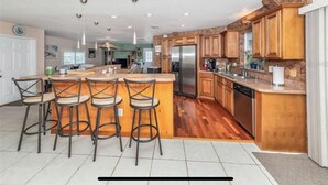A spacious kitchen with wooden cabinets, a central island with bar stools, a stainless steel refrigerator, and a dishwasher. - Gorgeous Pool house 5 min from the beach, shopping and restaurants I (Venice)