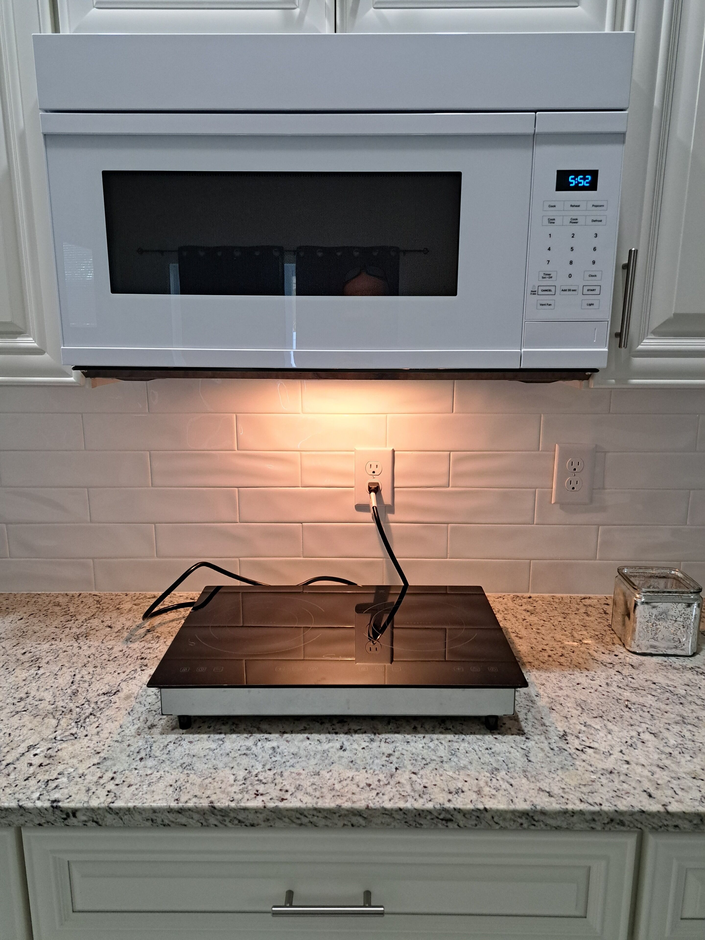 Una cocina con microondas, regadera y un recipiente de vidrio sobre la encimera.
