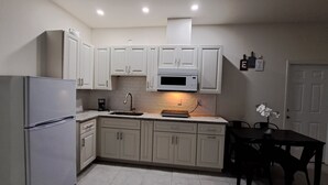 A compact kitchen with white cabinets, a built-in microwave, a refrigerator, and a dining area with a table and chairs. - New and luxurious (Tampa)