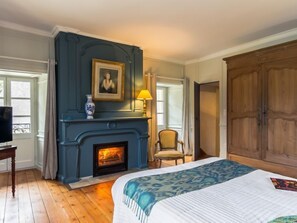 Une pièce avec une cheminée, un lit, une chaise, un téléviseur et une armoire.