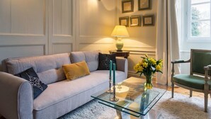 Een woonkamer met een bank, een glazen salontafel, een lamp, een stoel en een raam met gordijnen.