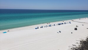 A beach with white sand, clear turquoise water, and a few umbrellas and lounge chairs.