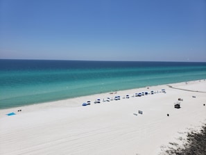 Une plage de sable blanc, avec une eau turquoise et limpide, quelques parasols et des chaises longues.