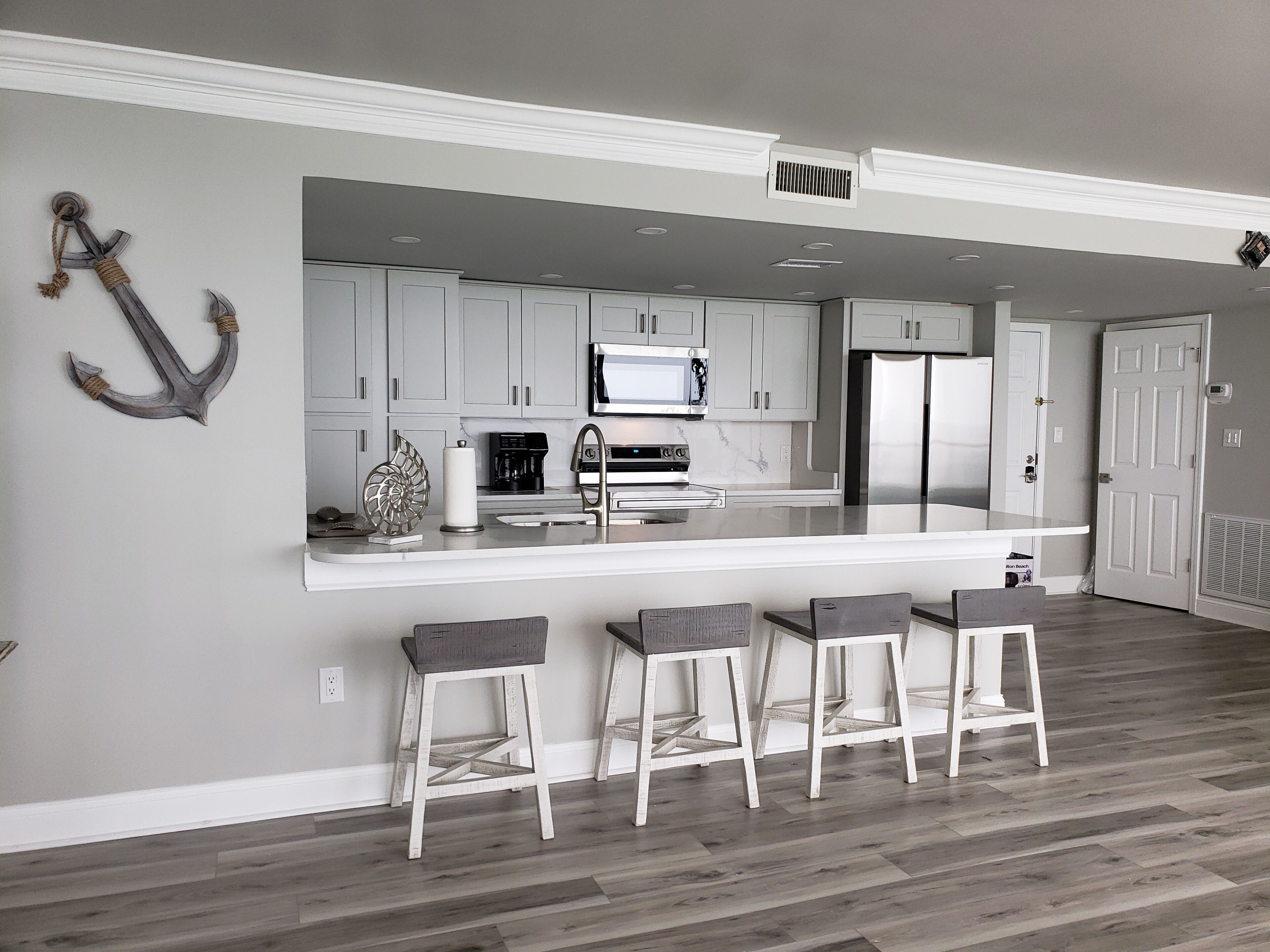 A modern kitchen with grey cabinets, a stainless steel refrigerator, a microwave, and a large island with bar stools.