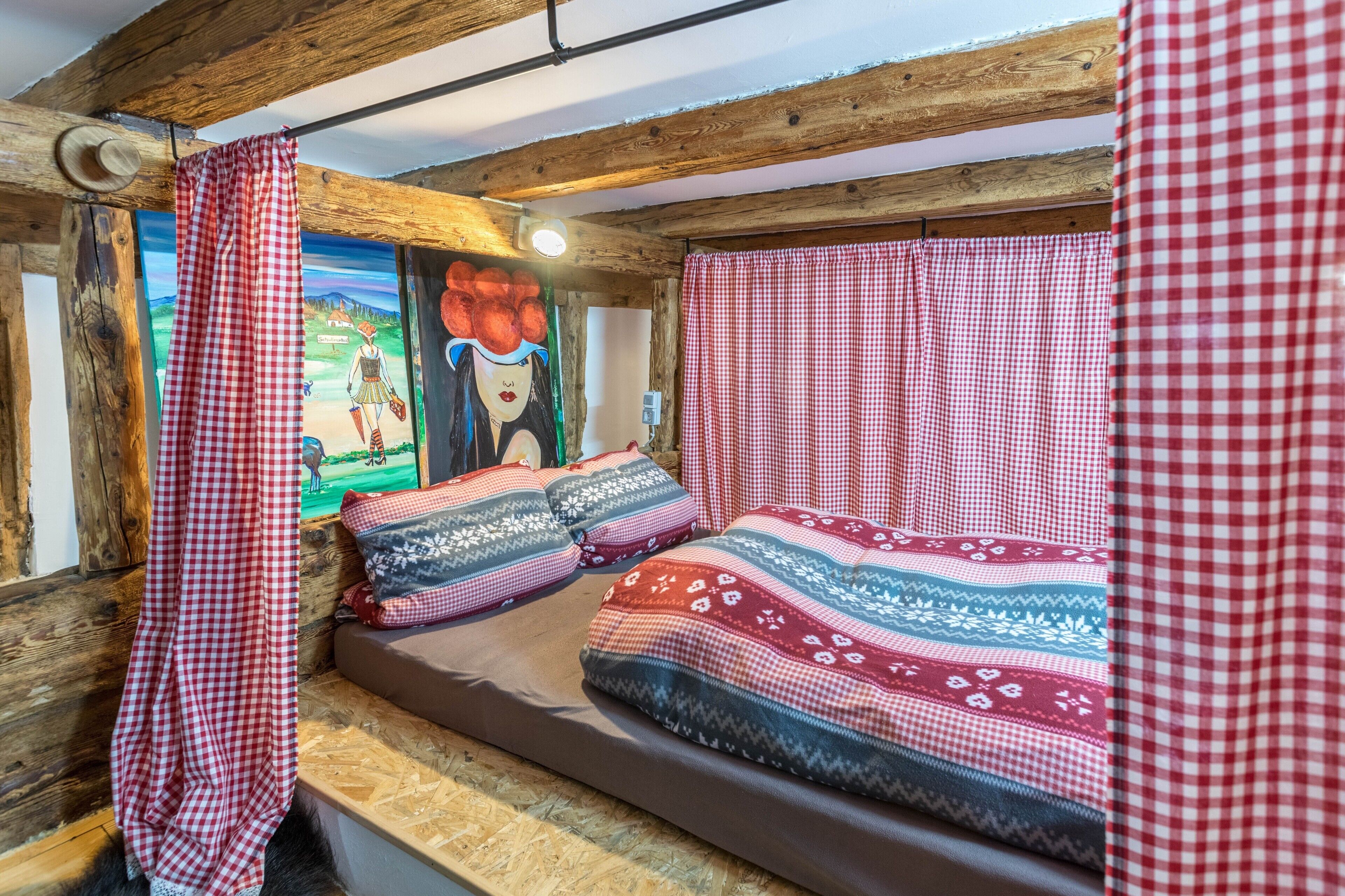 Ein gemütliches Zimmer mit Holzbalkendecke, einem Bett mit gemusterten Betttextilien und einem karierten Vorhang.