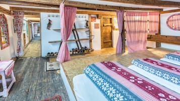 Ein rustikaler Raum mit Holzbalken, karierten Vorhängen, einem Bett mit gemusterten Textilien, einer Holzleiter und einem Wandregal mit Stiefeln.