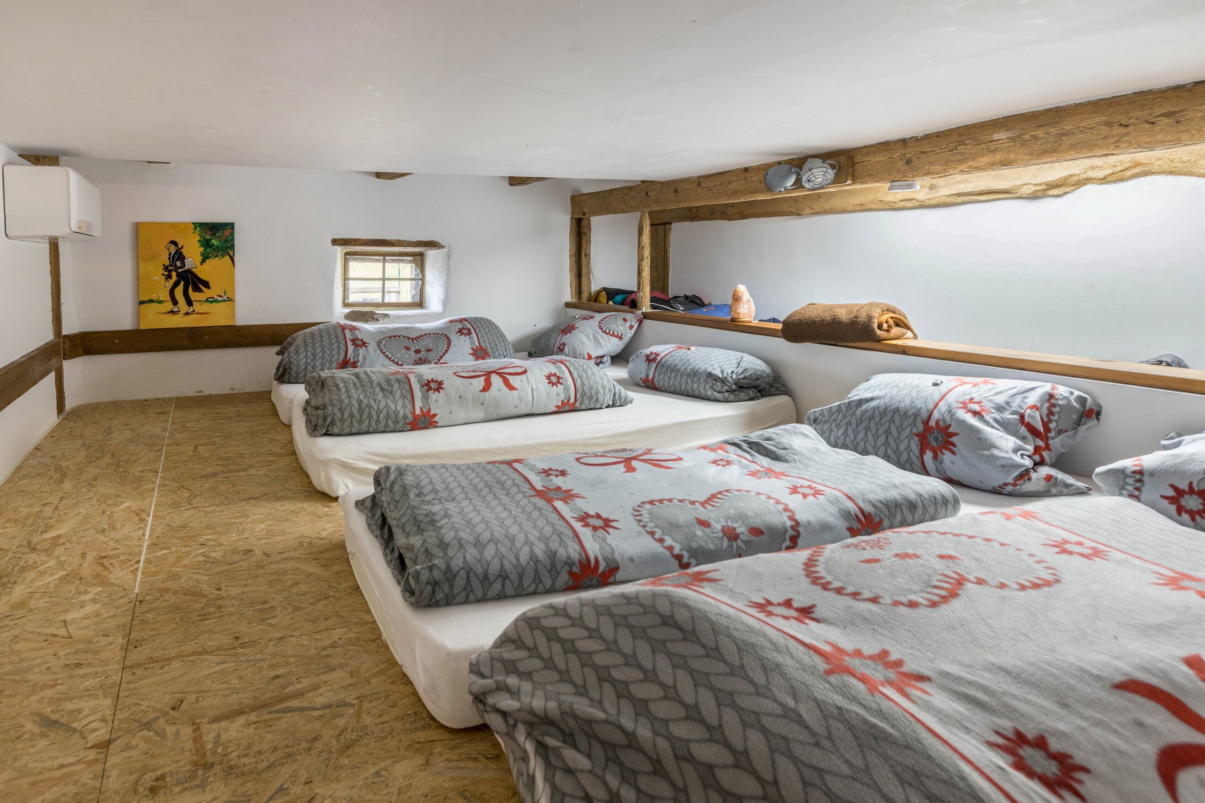 A room with three beds, a wooden ceiling, a window, and a painting on the wall.