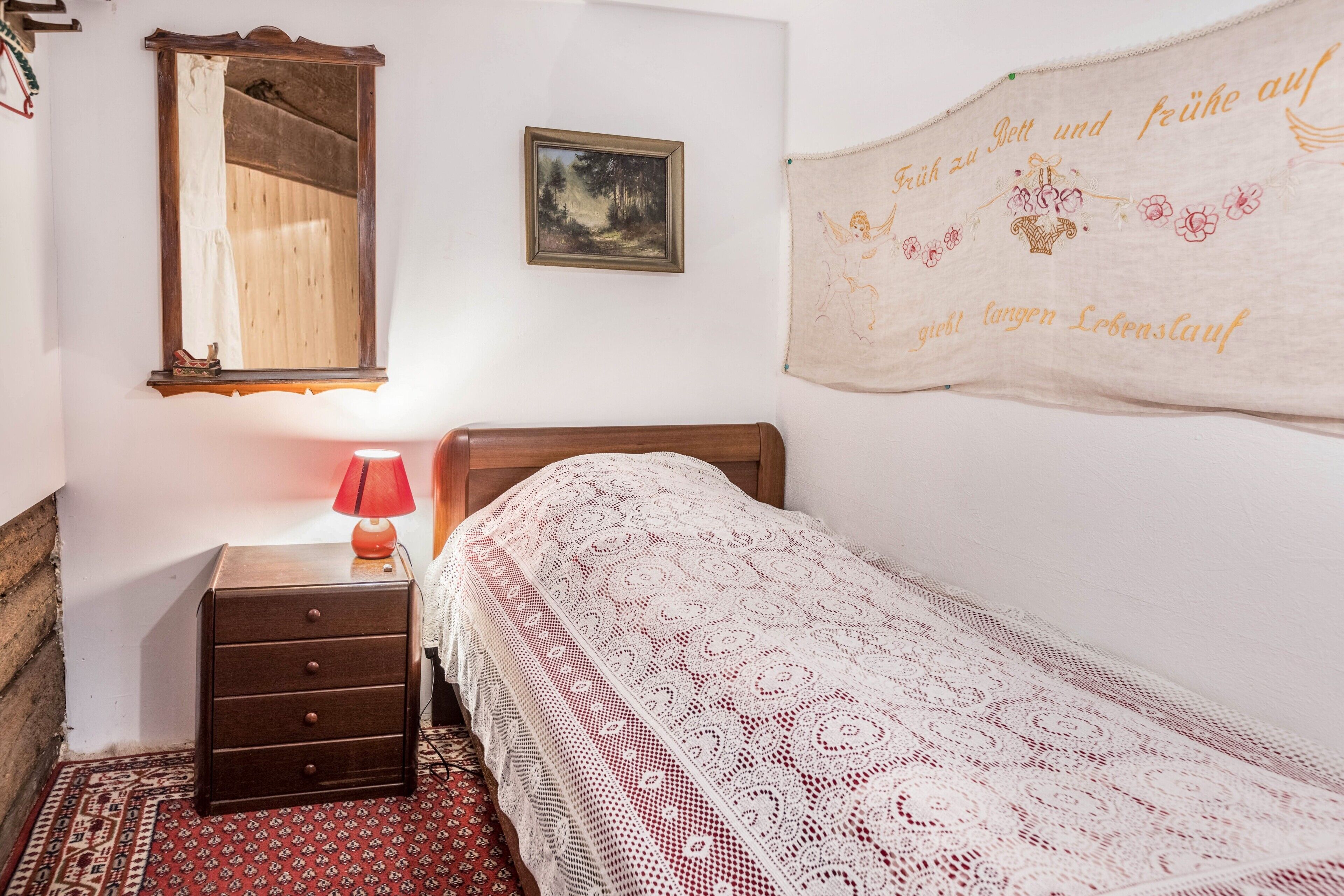 Una camera da letto con un letto in legno, un comodino con una lampada, uno specchio, un quadro incorniciato e un elemento decorativo a parete.