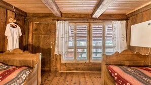 Una habitación de madera con dos camas, una ventana con cortinas y una pizarra en la pared.