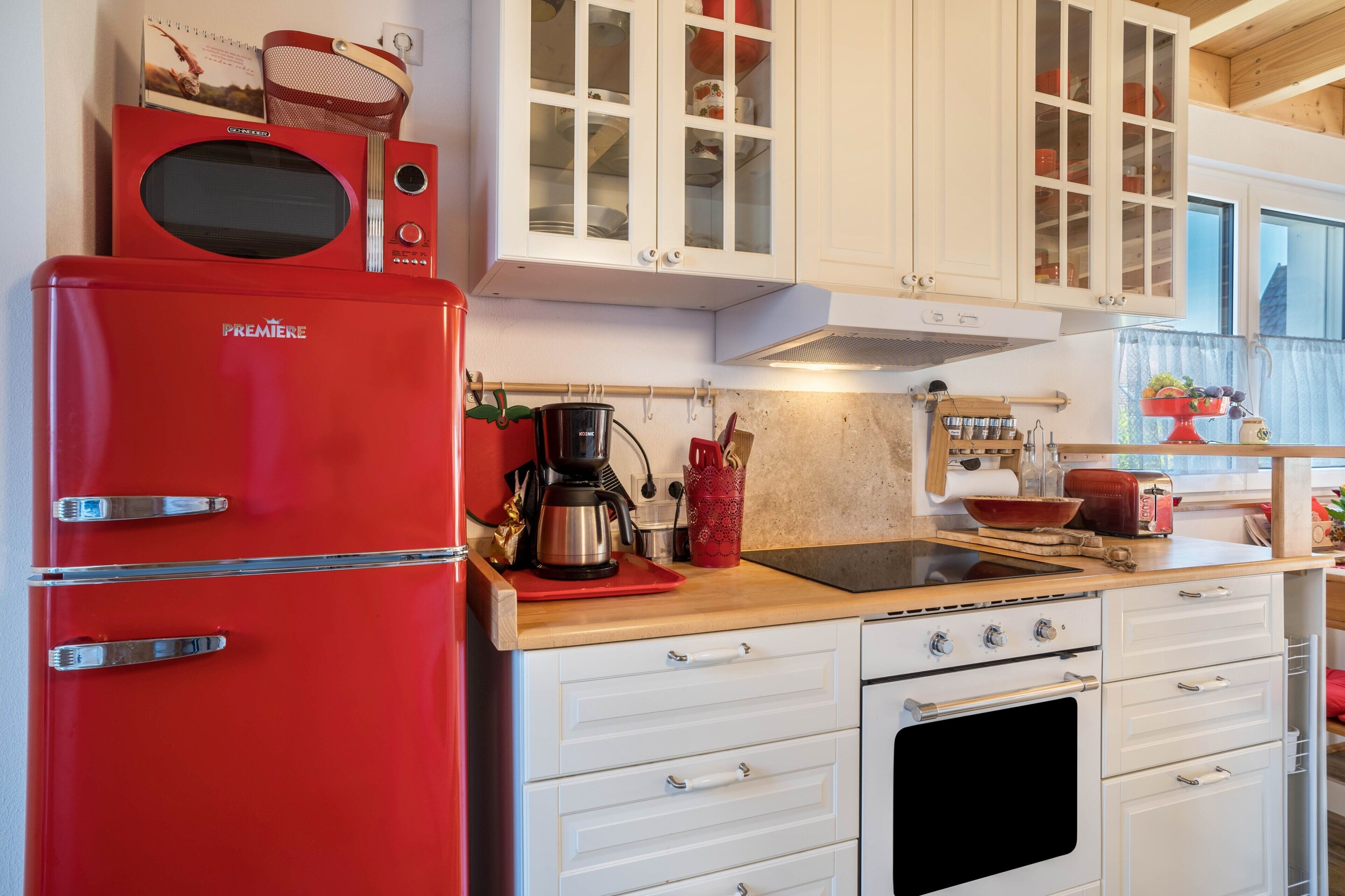 A kitchen with white cabinets, a red refrigerator, a coffee maker, and a stove.