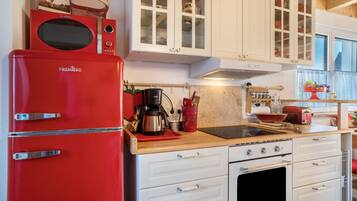A kitchen with white cabinets, a red refrigerator, a coffee maker, and a stove.
