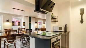 Een moderne keuken met een magnetron, een eethoek met houten stoelen, een centraal kookeiland en een hangende lamp.