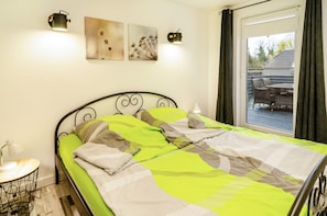 Ein Bett mit einer grünen und beigefarbenen Bettdecke, ein Nachttisch mit Lampe sowie ein an der Wand befestigtes Kunstwerk.