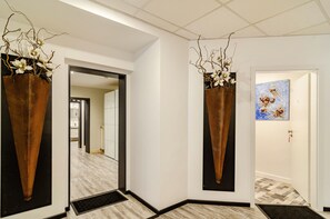 Un pasillo de diseño moderno, con un jarrón grande con ramas y flores, una puerta con un cuadro y un espejo grande en la pared.