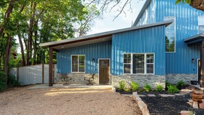 A blue metal house with a stone foundation, a gravel driveway, and a small garden with rocks and plants. - Heart of Kanab Home (Kanab)