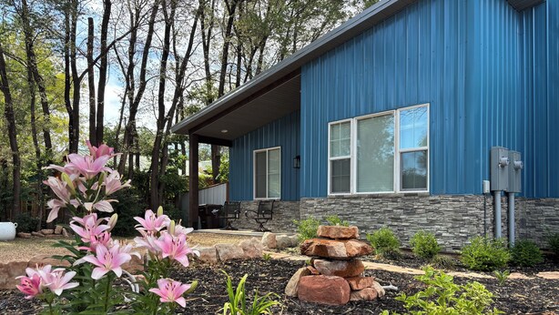 A modern house with a blue exterior, stone foundation, and a garden with pink lilies and rocks. - Heart of Kanab Home (Kanab)