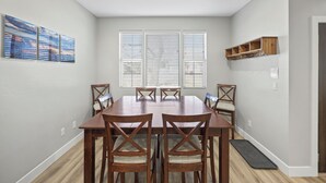 A dining room with a wooden table and chairs, large windows with blinds, and a wall-mounted shelf with hooks. - Heart of Kanab Home (Kanab)