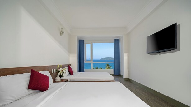 Quarto de hotel com duas camas, televisão e janela com vista para o mar.