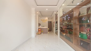 Corredor de hotel com balcão de recepção, uma placa com a inscrição "NAMI Hotel" e uma vitrine de bolsas.
