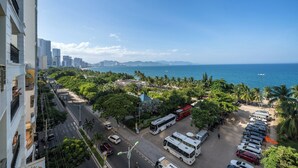 Paisagem costeira com vista para o mar, área de estacionamento com ônibus e uma estrada ladeada por árvores e edifícios.