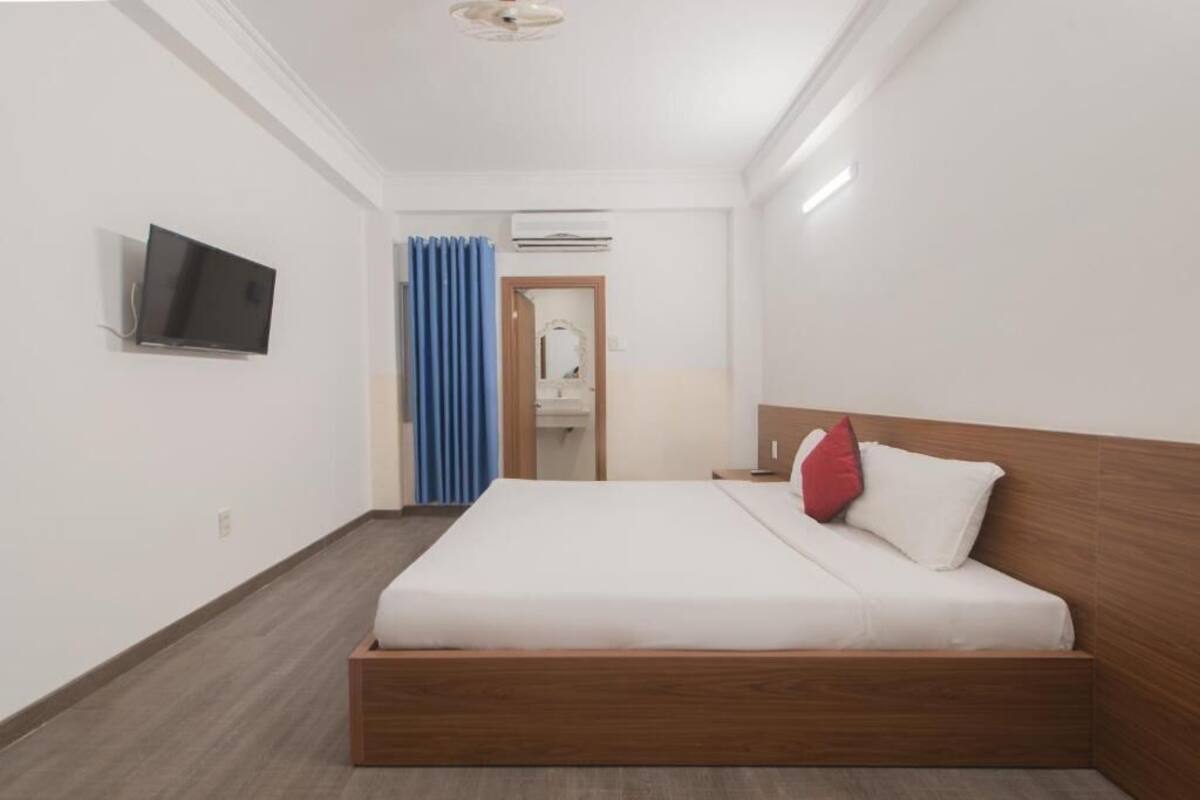 A hotel room with a wooden bed, a flat-screen TV, a mirror, and an air conditioning unit.