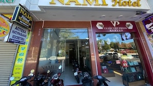 Entrada do Hotel NAMI com fachada de vidro, placa de loja de cosméticos e várias motocicletas estacionadas.