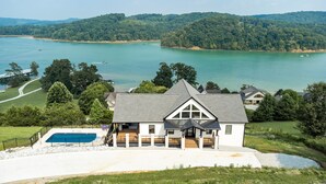 Una casa grande con piscina, rodeada de césped cuidado y vistas a un lago.