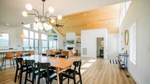 Un comedor espacioso con una larga mesa de madera y sillas negras, una lámpara moderna y ventanas amplias que dejan entrar luz natural.