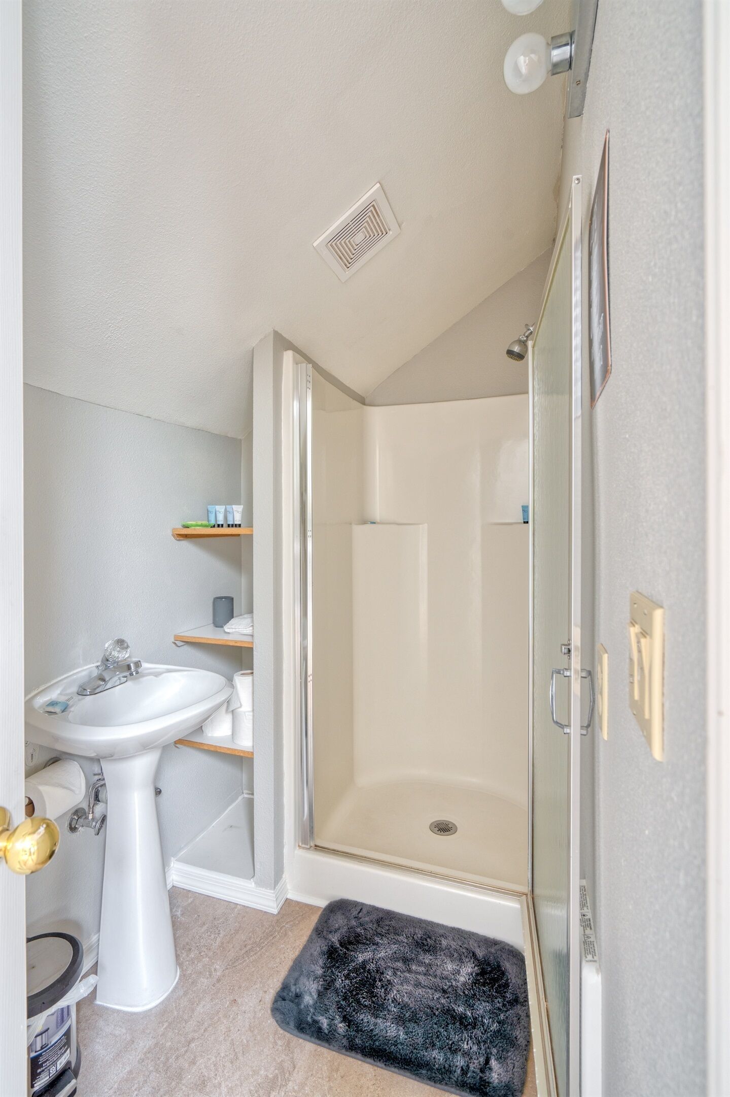 A bathroom with a white sink, a glass shower enclosure, and a small step leading to the shower.