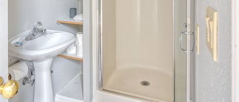 A bathroom with a white sink, a glass shower enclosure, and a small step leading to the shower.
