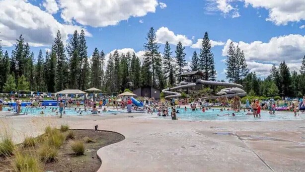Un parc aquatique doté de plusieurs piscines et de toboggans, entouré de grands arbres.
