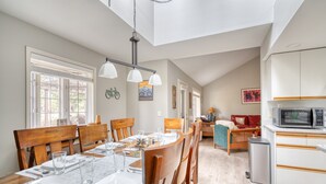 Un coin repas avec une table en bois dressée pour quatre personnes, une cuisine avec des meubles blancs et, au fond, un canapé rouge.